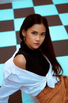 Striking portrait of a young woman in modern fashion sitting on a blue and black checkered floor.