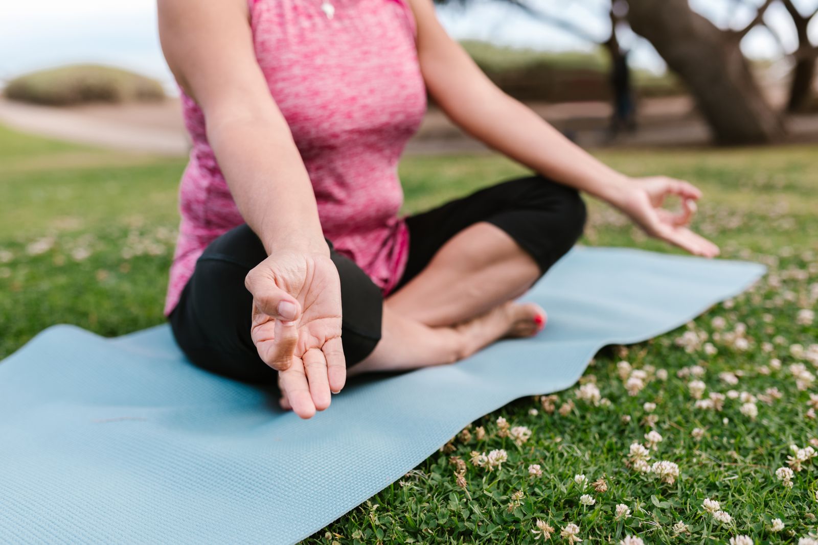 Woman practicing a hand mudra while seated on a yoga mat outdoors