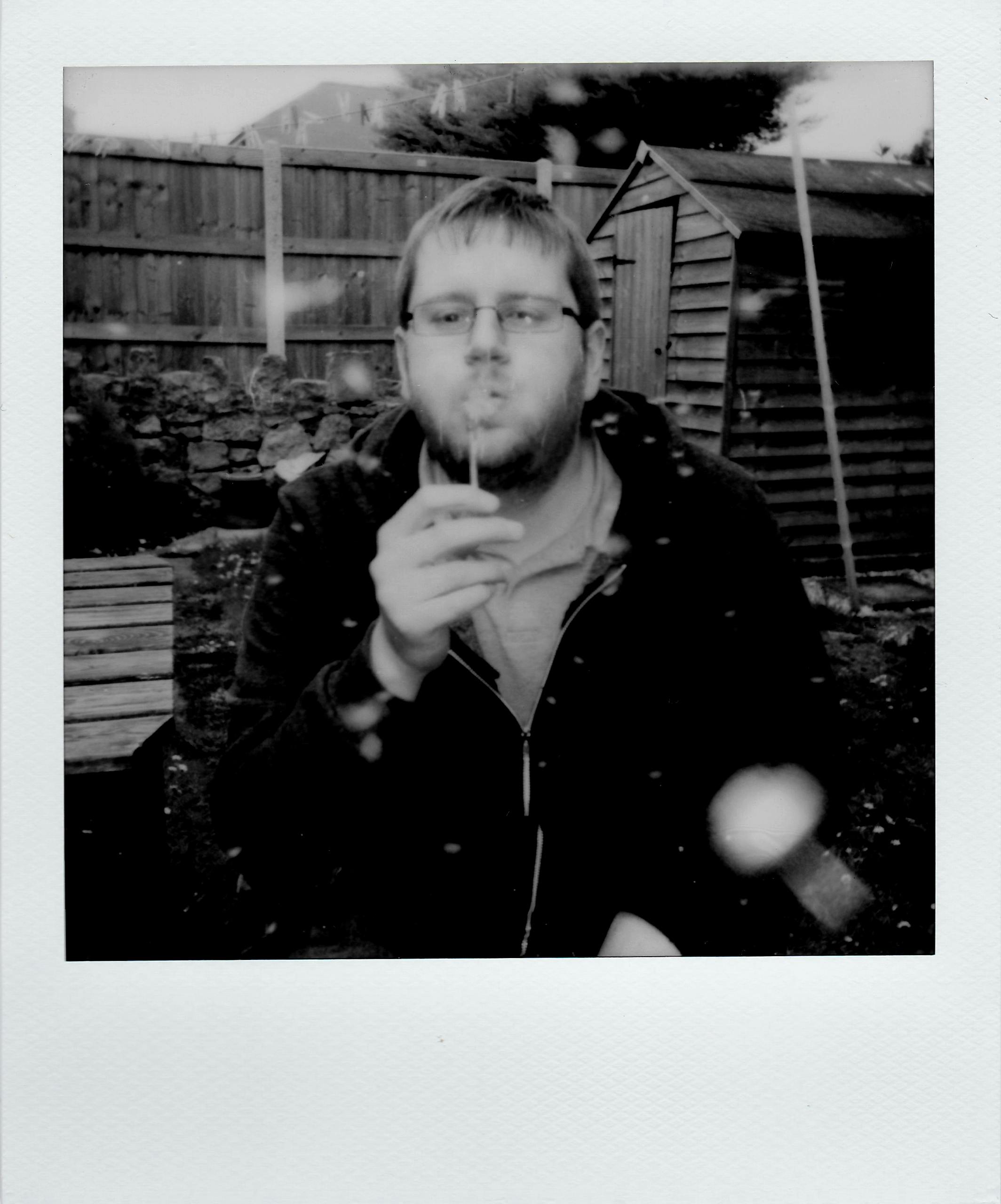 A man enjoying blowing soap bubbles in a vintage-style garden setting, captured in black and white.