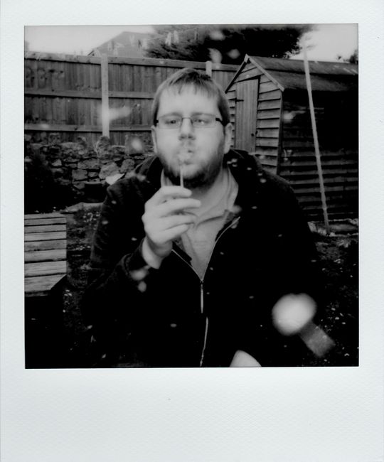 A man enjoying blowing soap bubbles in a vintage-style garden setting, captured in black and white.