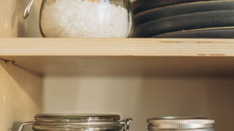 Close-up of pantry shelves with glass containers holding walnuts, salt, and preserves.