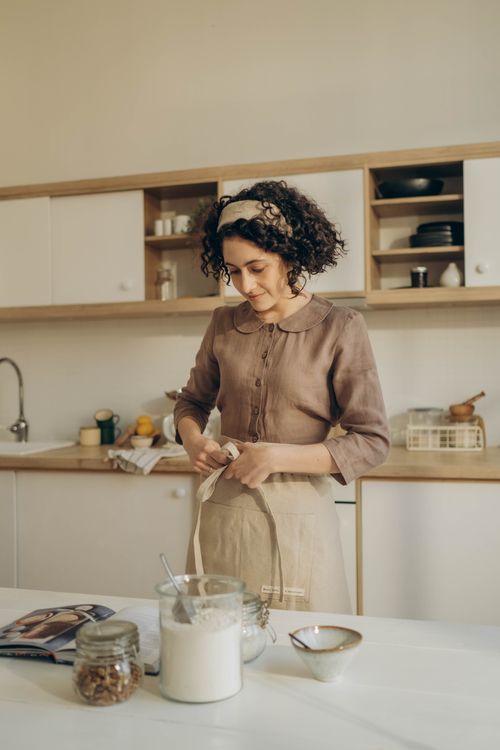 Free Woman with curly hair baking in a cozy home kitchen, tying apron. Stock Photo