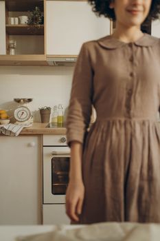 Woman in a brown dress standing in a cozy kitchen setting.