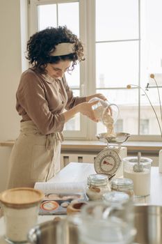 A woman measuring ingredients with a scale in a cozy kitchen setting, perfect for culinary content.