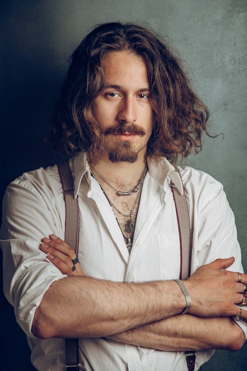 Man with a Beard Wearing Suspenders Standing with his Arms Crossed