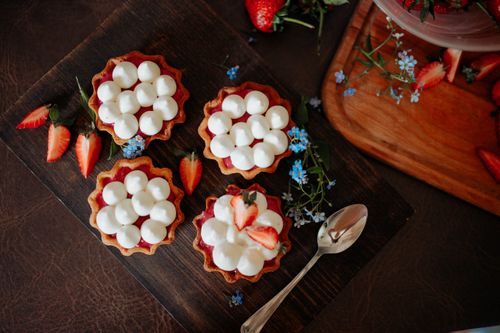Free From above of delicious cookies decorated with cream and strawberries placed on wooden board with spoon and flowers on table in kitchen Stock Photo