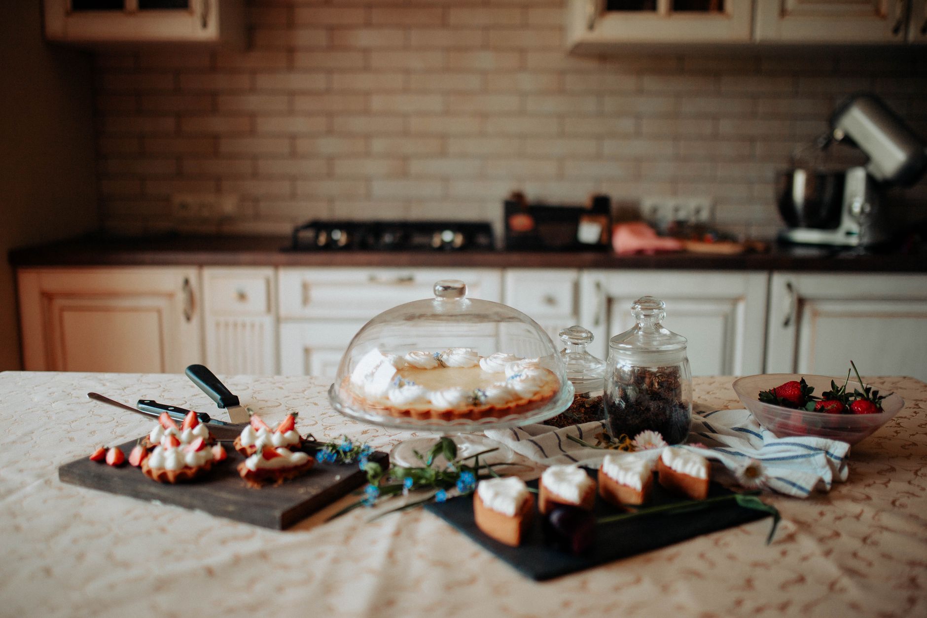 Mesa de madeira em cozinha acolhedora com potes de sobremesas simples, morangos e creme, iluminadas por luz quente de abajur