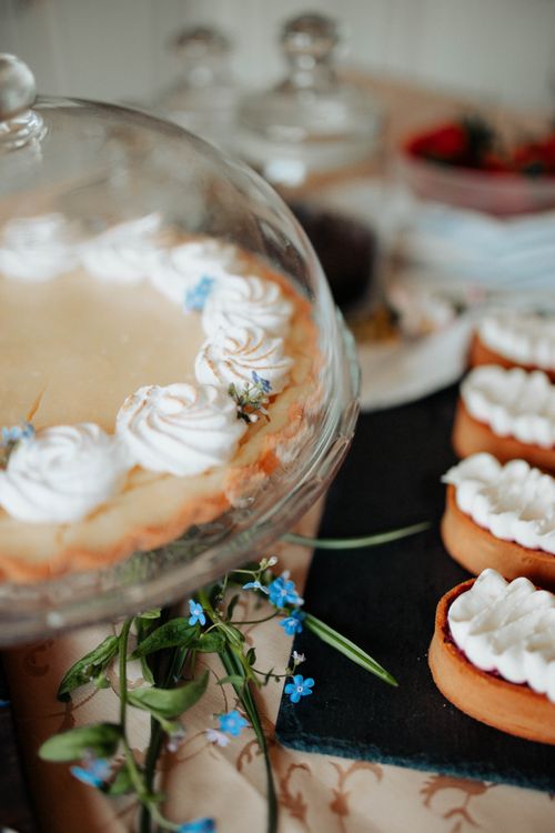 Free Tart with cream on tray with glass cap on counter near desserts and flowers in light kitchen Stock Photo