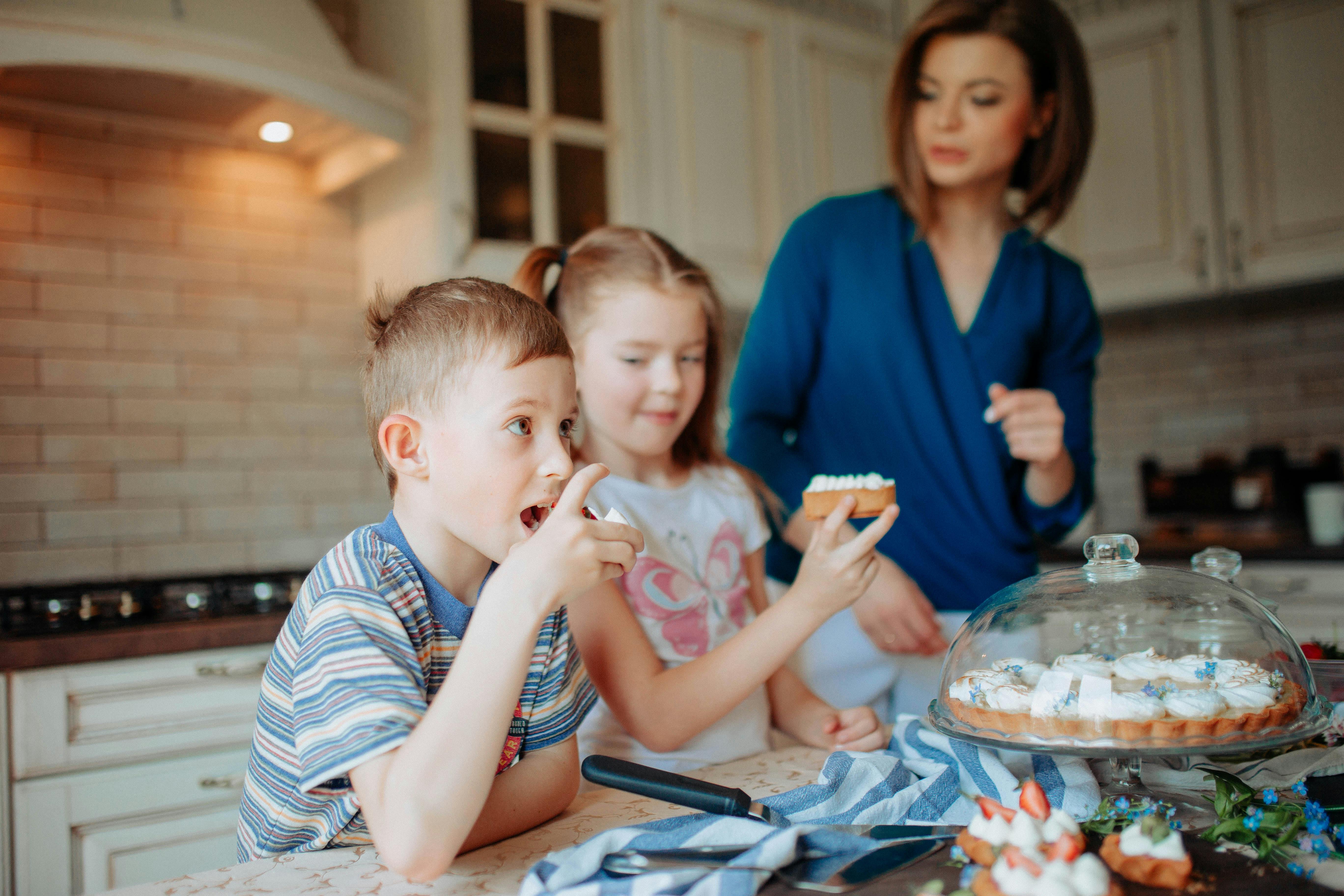 children with female at table with various desserts in kitchen