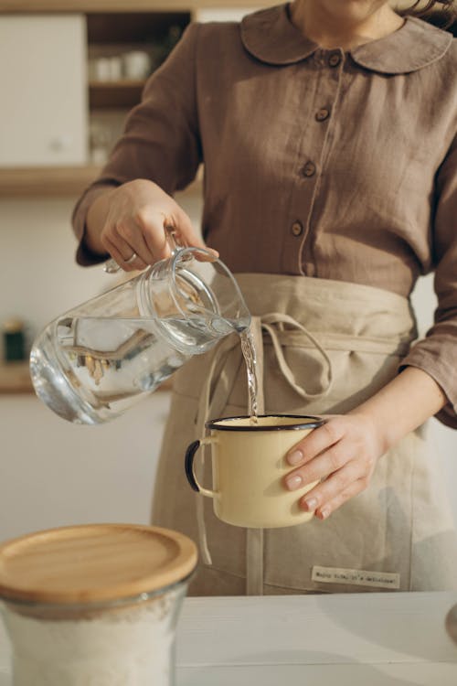 Woman in apron putting pouring water in cup