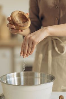 Woman sprinkles salt into a stainless steel bowl in a kitchen setting.