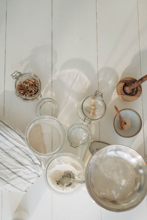 Free A top view of baking ingredients and tools on a white wooden surface, featuring flour, nuts, and kitchen utensils. Stock Photo