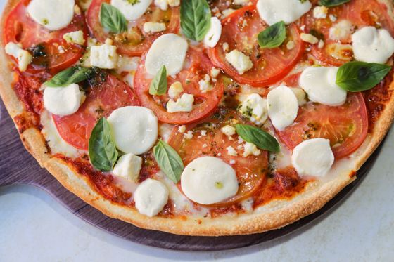 Thin-crust pizza topped with tomato slices, fresh mozzarella rounds, feta crumbles and basil