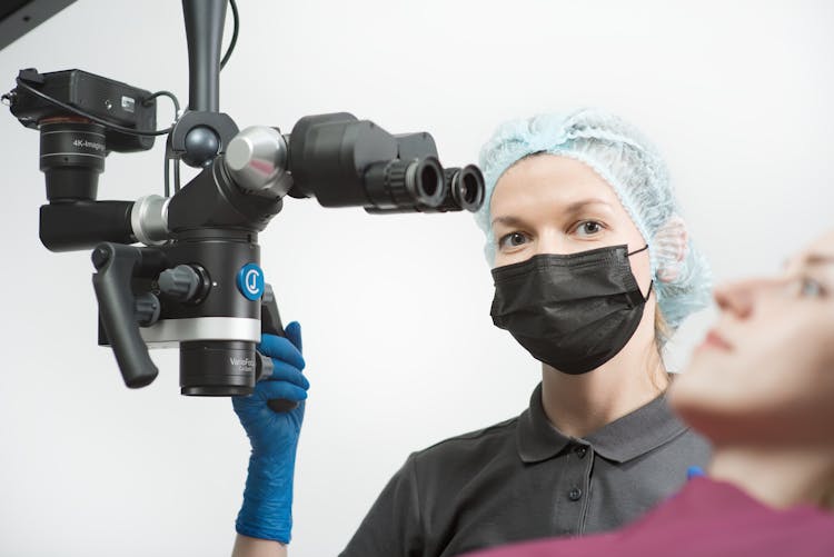 A Woman Wearing A Hair Net And A Facemask Holding A Medical Equipment