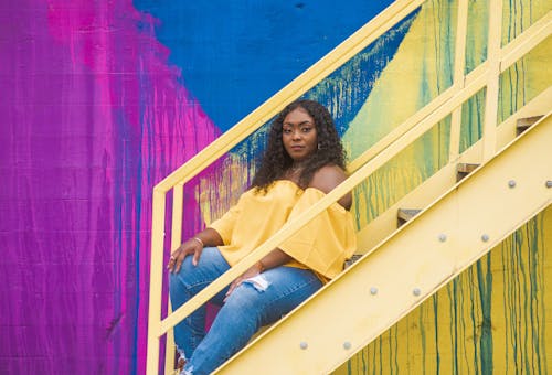 Free Woman in Yellow Top and Blue Denim Jeans Sitting on Yellow Stairs Stock Photo