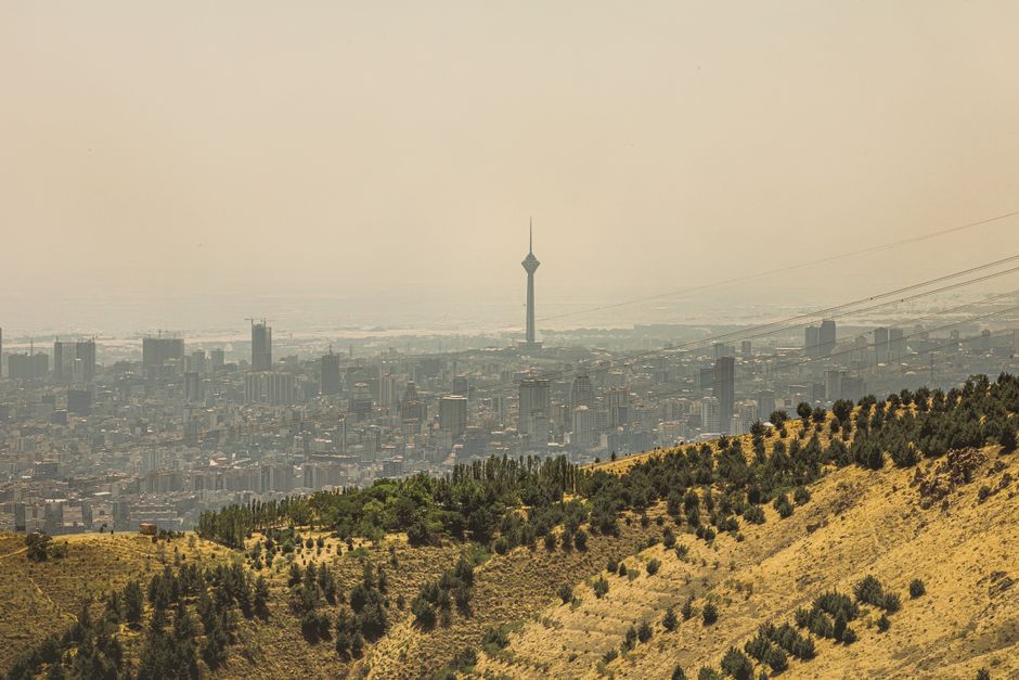 View of Tehran cityscape featuring the Milad Tower surrounded by hills under hazy skies.