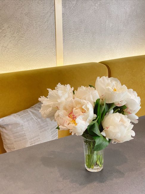 A stylish arrangement of white peonies in a glass vase on a table indoors, with a warm backdrop.