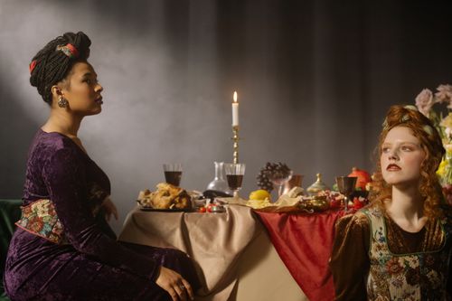 Free Elegant dining scene with two women in vintage fashion attire surrounded by a lavish feast. Stock Photo