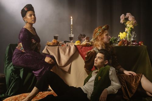 Free A theatrical setting of people in lavish renaissance costumes lounging around a candlelit table. Stock Photo
