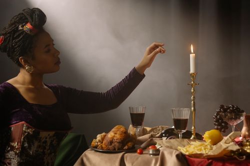 Free A woman enjoying a renaissance-inspired dinner setting with candles and vintage decor. Stock Photo