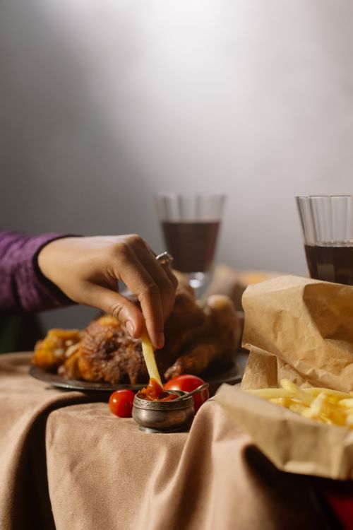 Free A hand dips a fry into ketchup, surrounded by fries and meat dishes, with glasses of wine in a cozy setting. Stock Photo