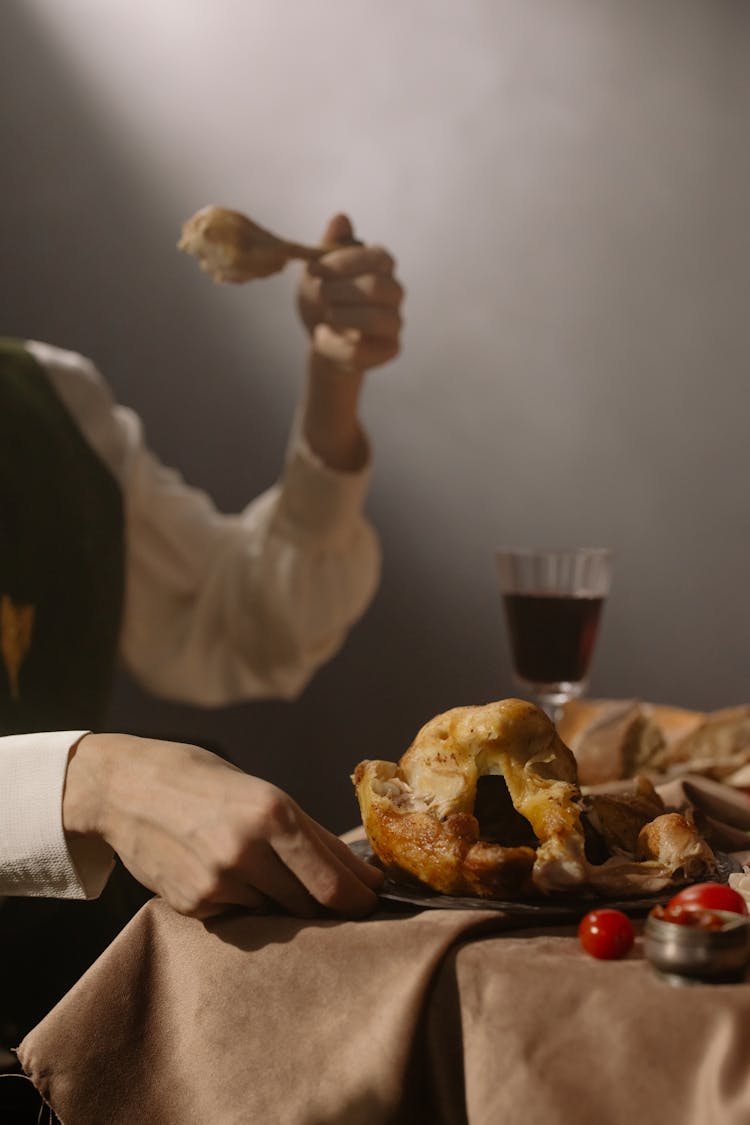 Person Holding A Piece Of Roast Chicken