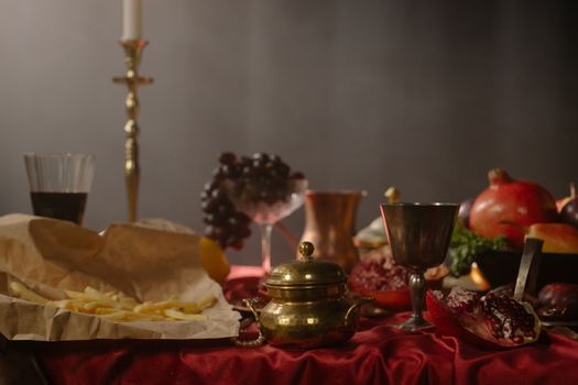 A classic still life featuring fries, goblets, and fruits on a red tablecloth.