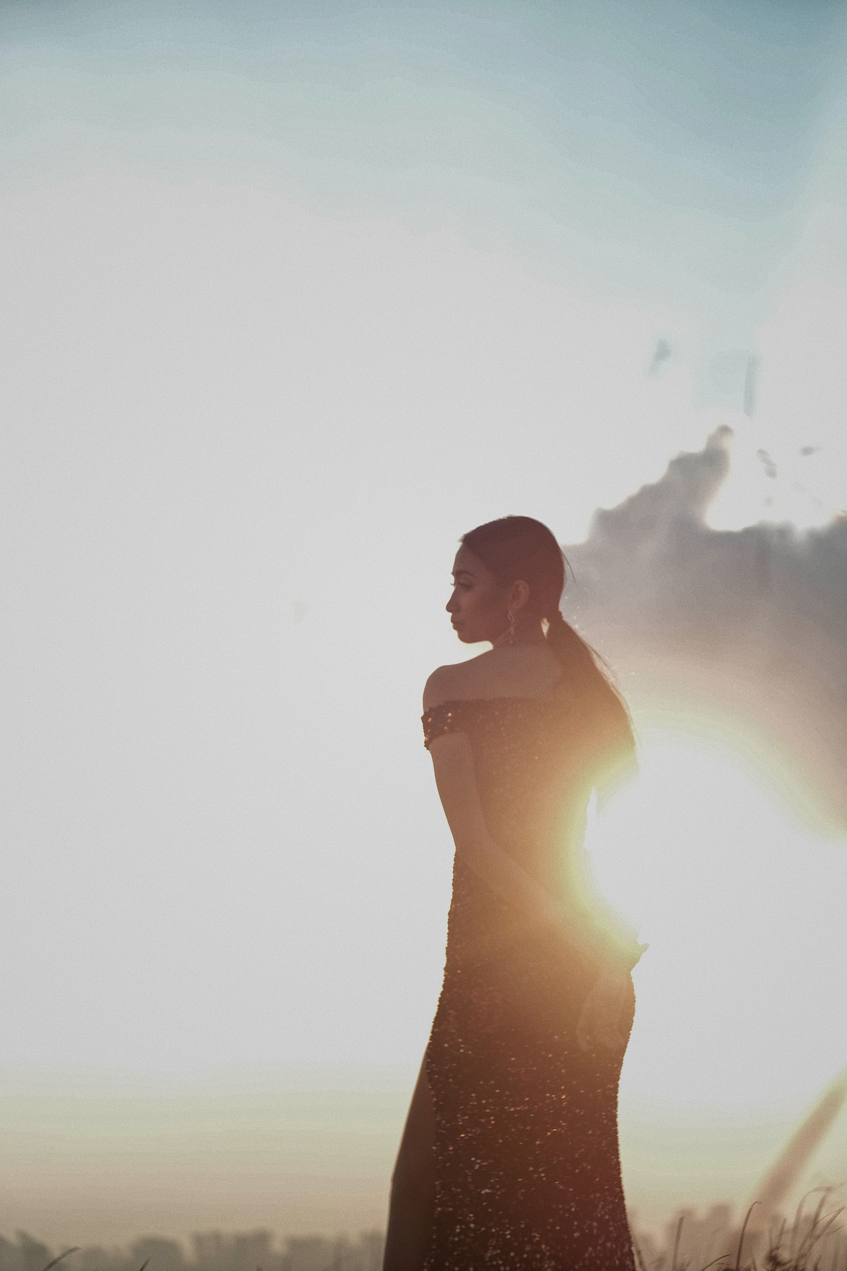 Silhouette in a glittering dress against sunset lens flare.