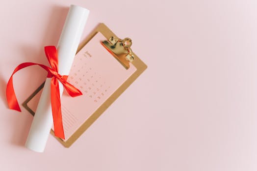 Rolled diploma with red ribbon on clipboard next to June calendar, perfect for graduation season themes.