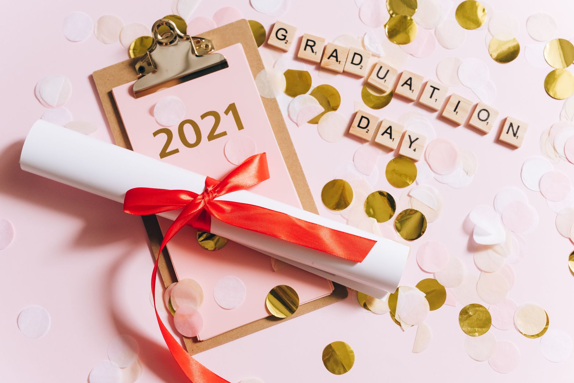 Festive graduation scene with diploma, confetti, and 2021 calendar on pink background.