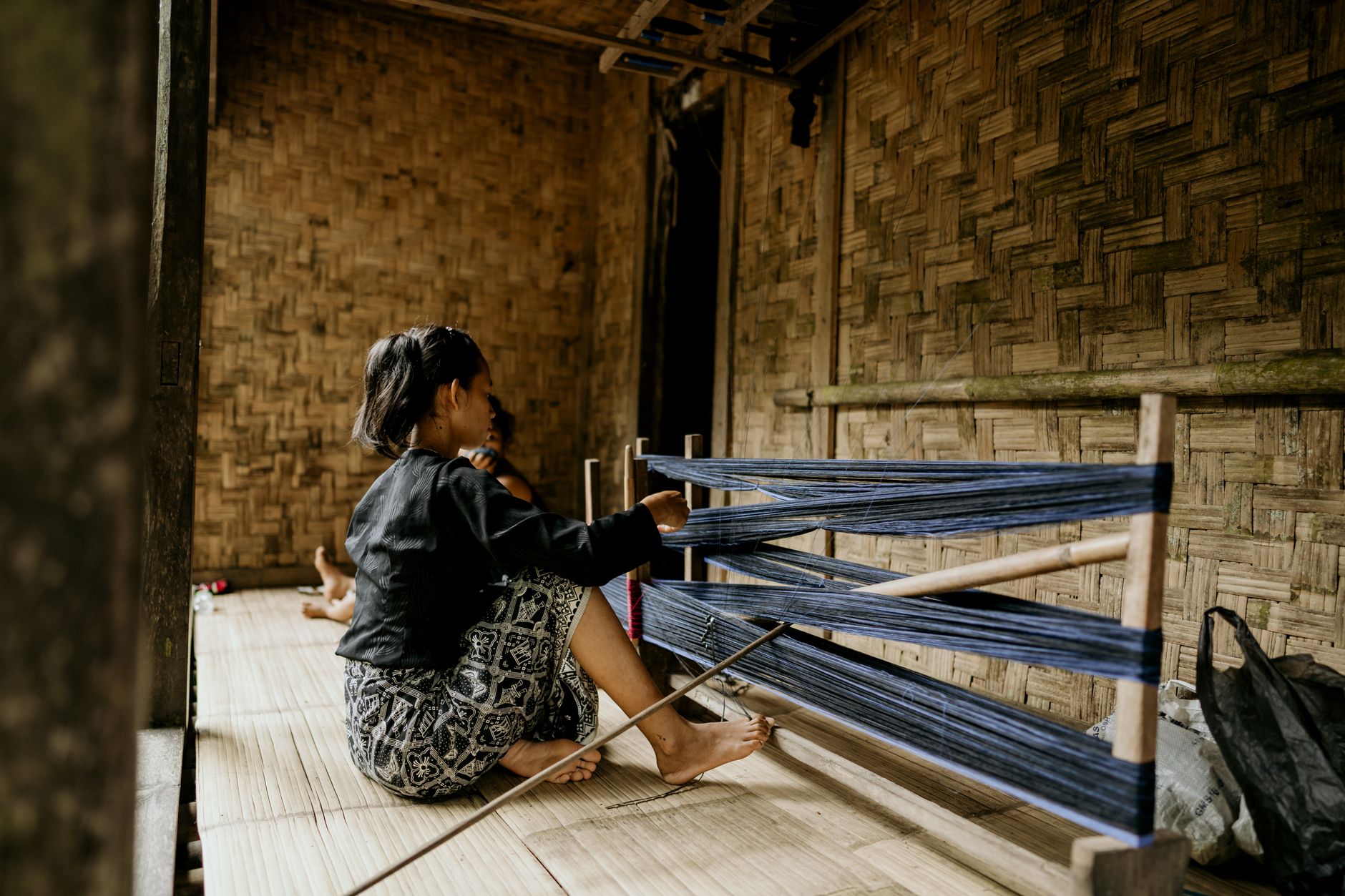 An adult woman weaving on a loom indoors in Banten, Indonesia.