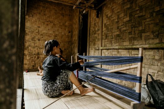 An adult woman weaving on a loom indoors in Banten, Indonesia.