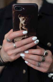 A detailed close-up of manicured hands holding a smartphone with a cute lion cub case.