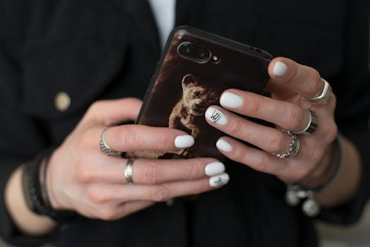 Close-up of hands with white nail polish holding a smartphone with a lion cub case indoors.