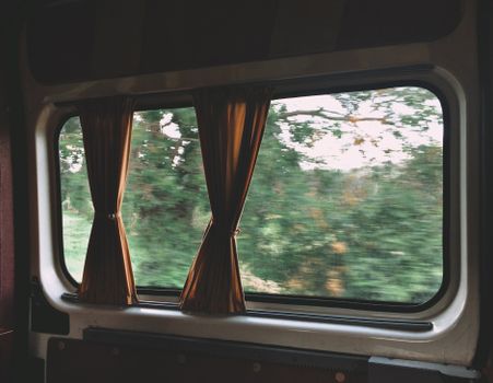 A serene view of lush greenery through a train window with curtains in Türkiye.