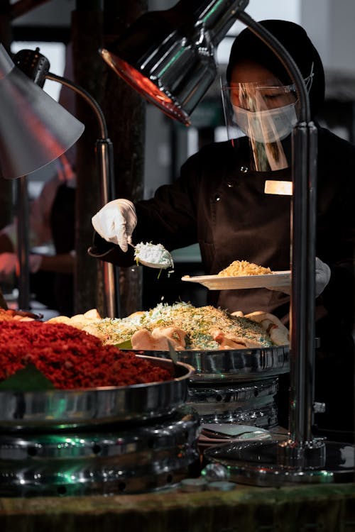 Person in Brown Long Sleeve Chef Uniform Preparing Food on Buffet Table