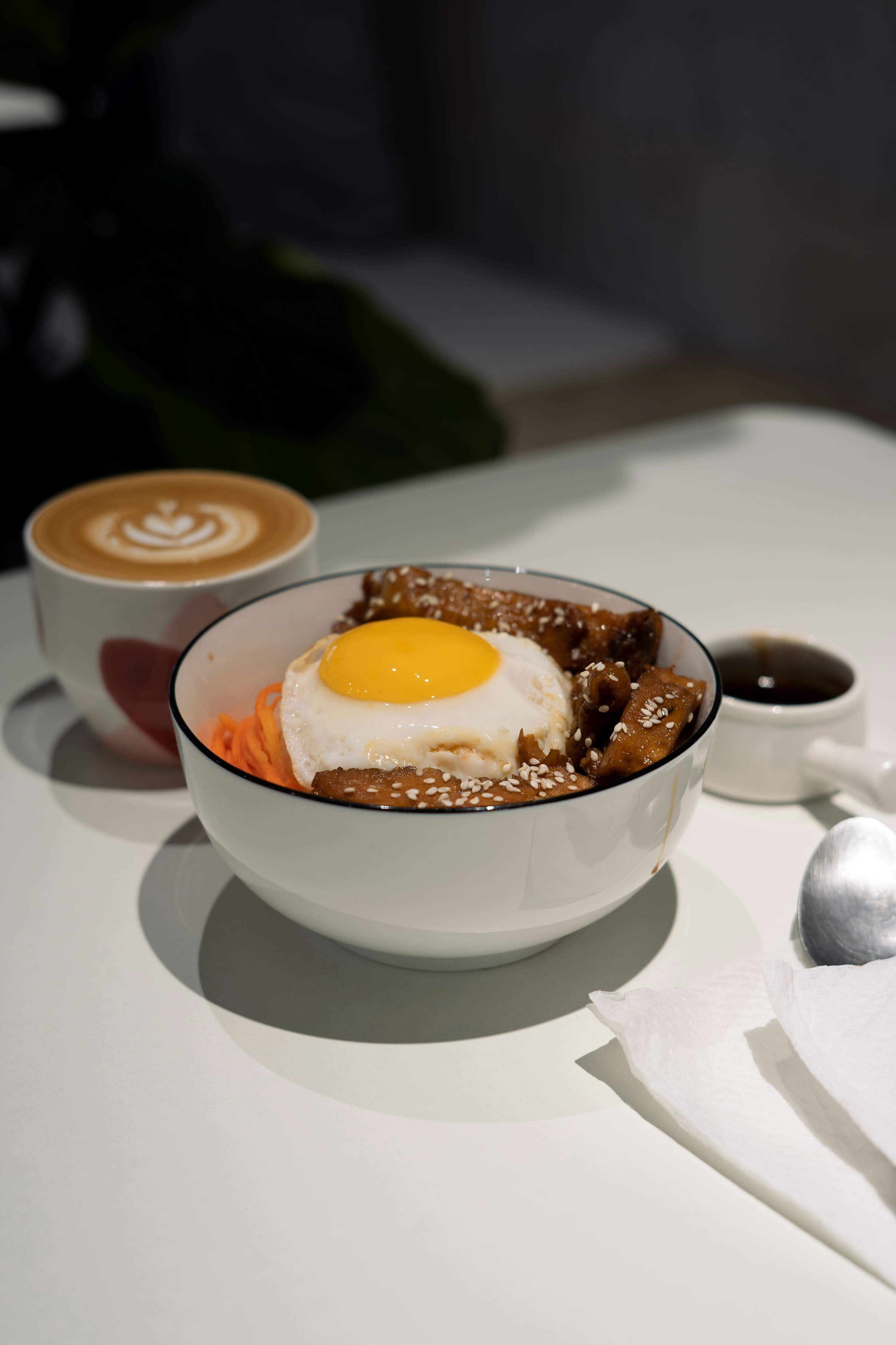 A tasty meal of noodles with egg and cappuccino on a white table setting.