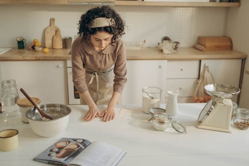 Woman in Brown Long Sleeve Shirt Standing beside White Kitchen Counter