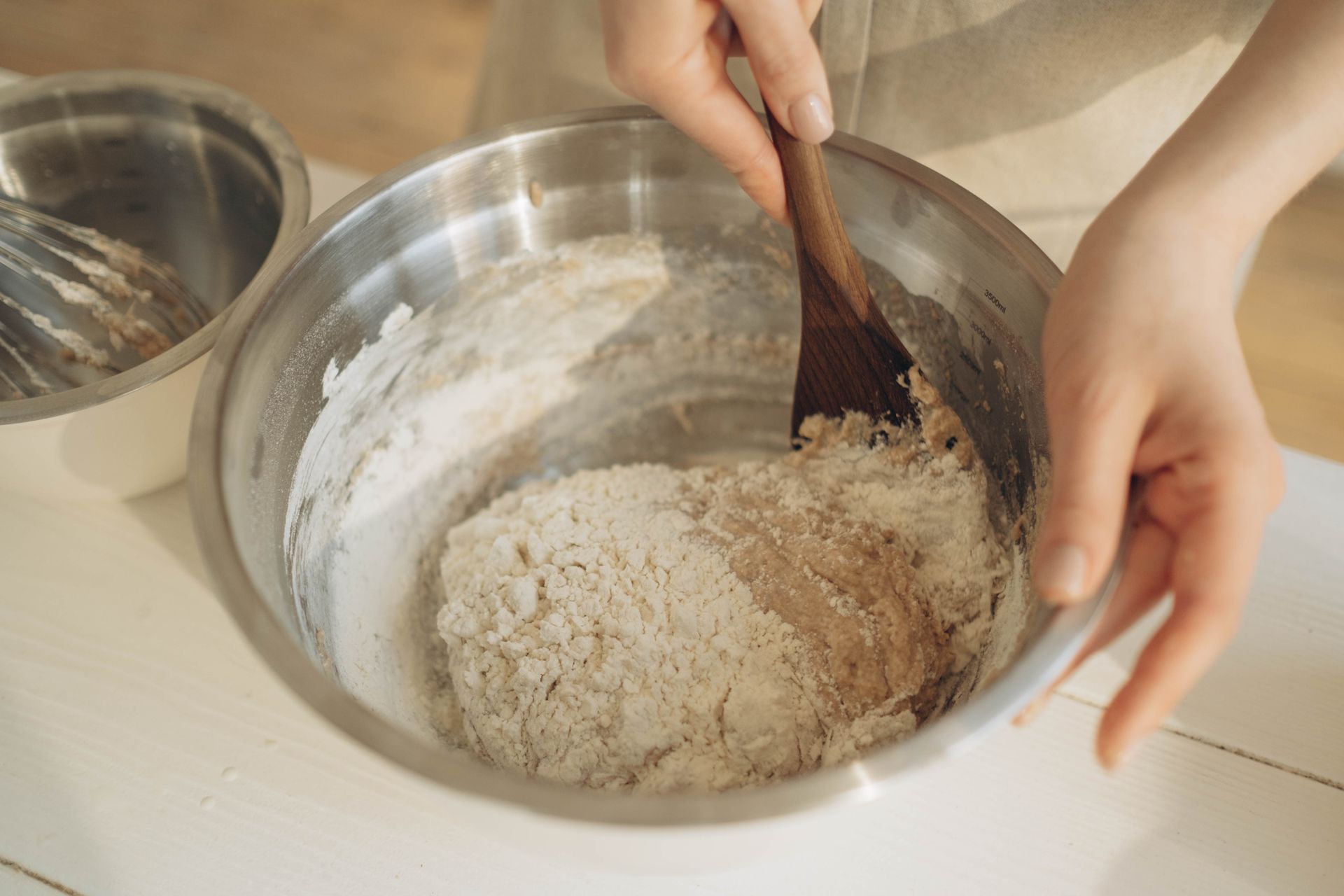 A Person Mixing the Dough Using a Wooden Spatula in a Stainless Bowl