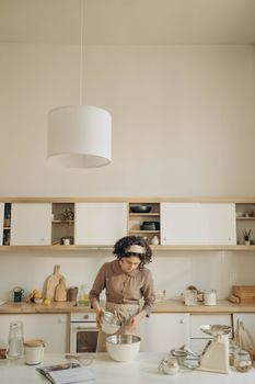 A woman prepares batter in a stylish kitchen with mixing bowls and utensils.