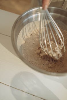 Close-up of mixing dough in a stainless steel bowl with a whisk.