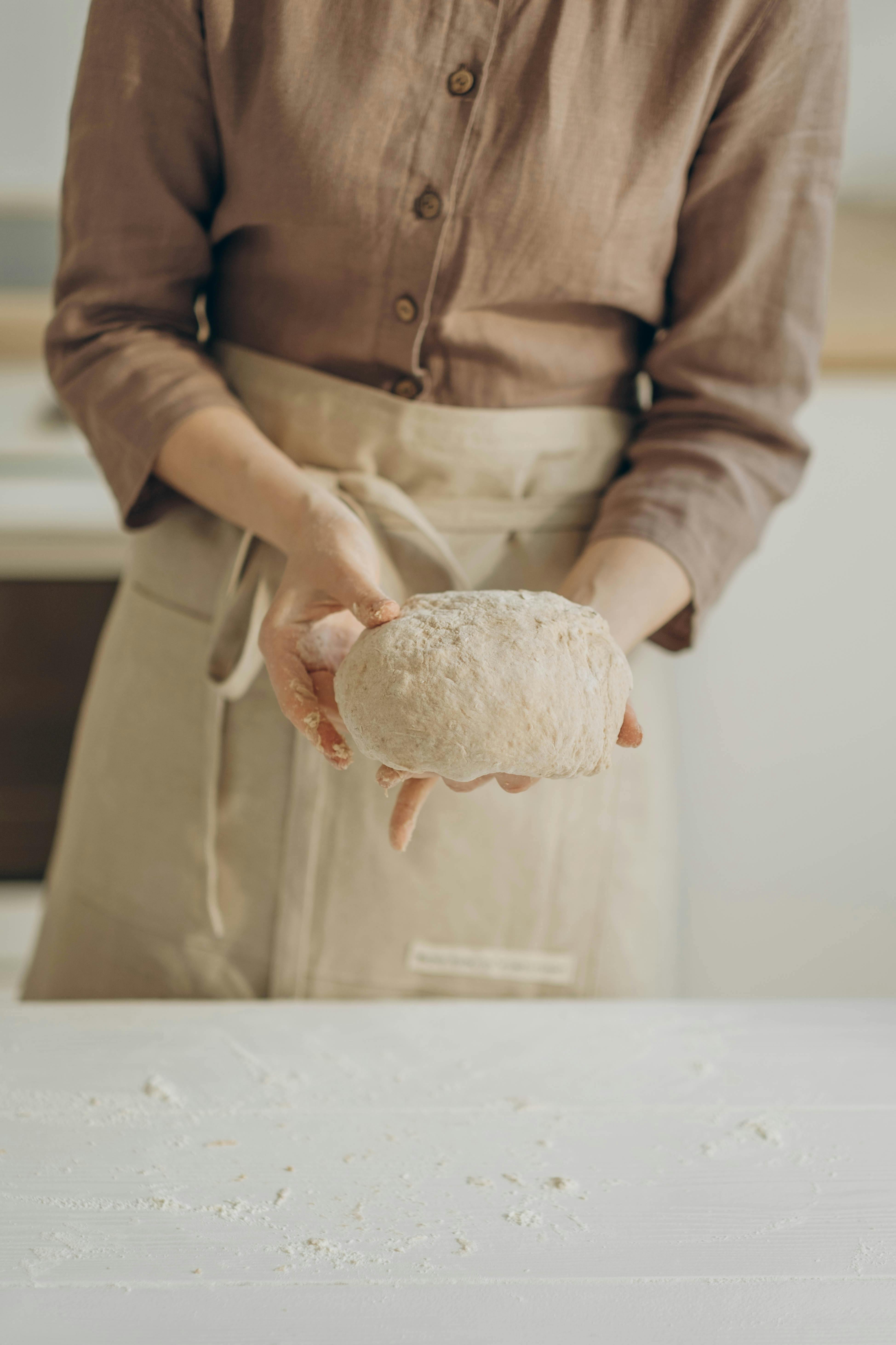 person in brown long sleeve shirt holding a dough