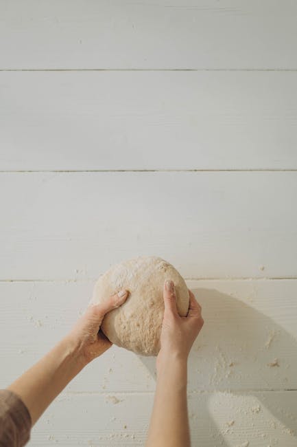 A close-up shot of hands kneading dough, with flour dusting the surface