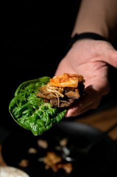 Hand holding Korean BBQ lettuce wrap with kimchi, showcasing vibrant flavors and textures.