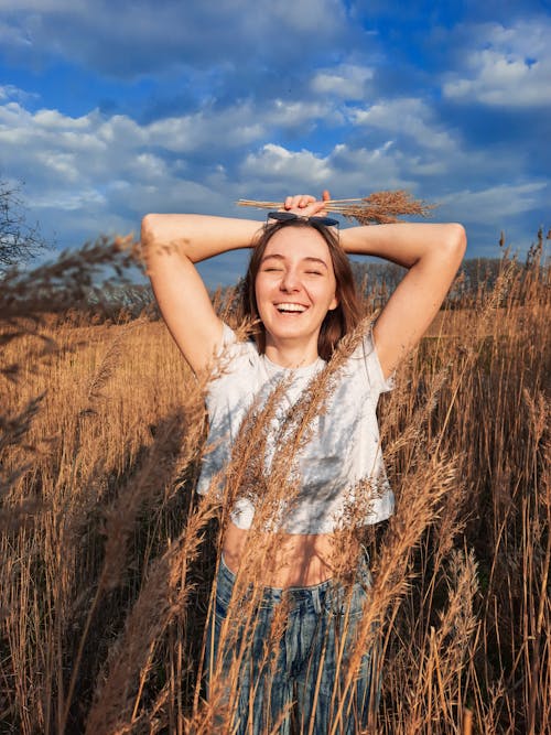 Photo of a Woman in a White Crop Top Laughing with Her Hands on Her Head