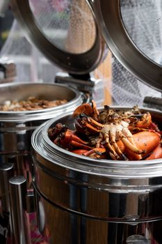 Mouth-watering crabs in a stainless container at a seafood buffet, captured in a vertical shot.
