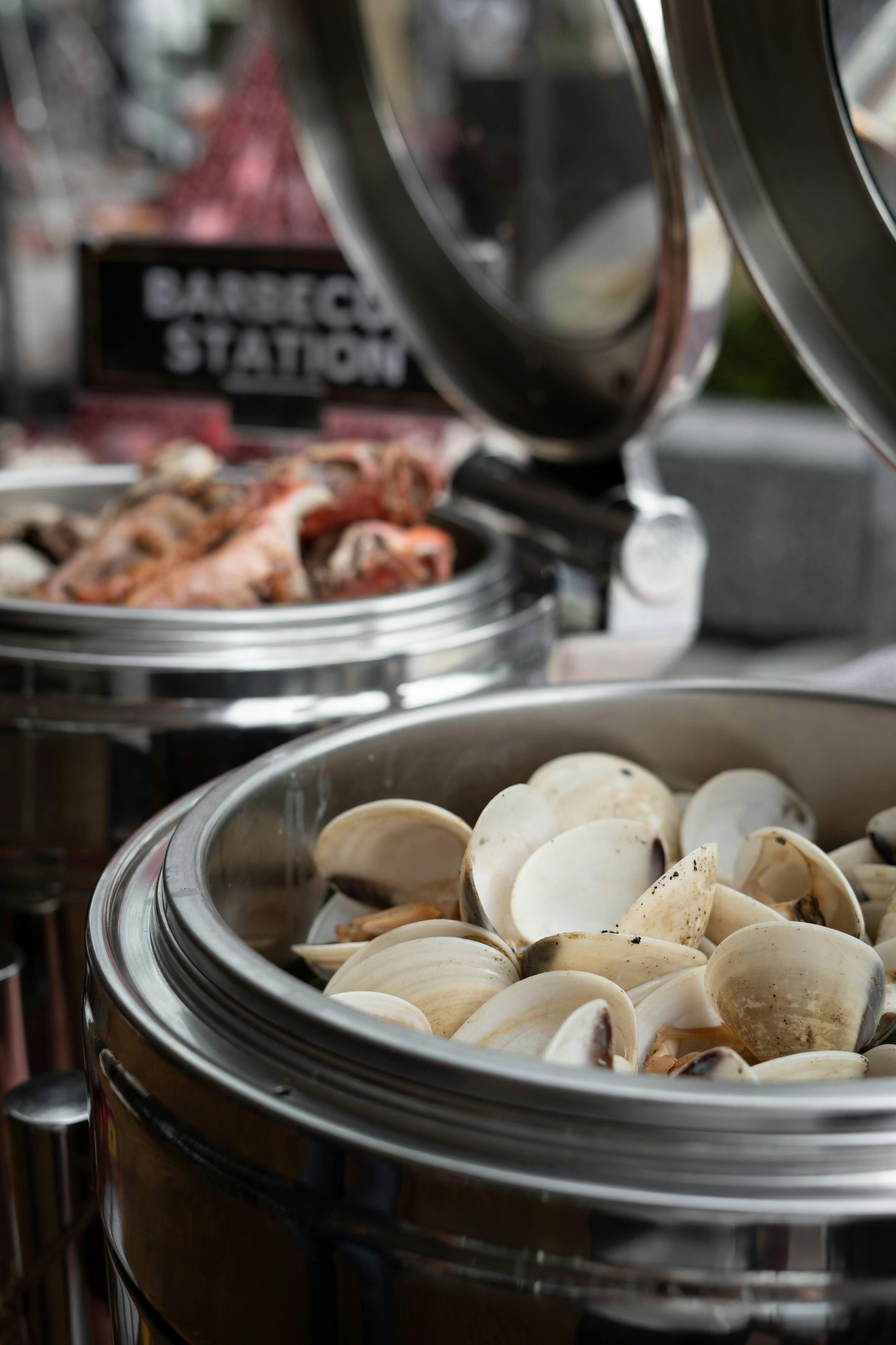 A close-up view of clams and shrimp in food warmers at a seafood buffet station.