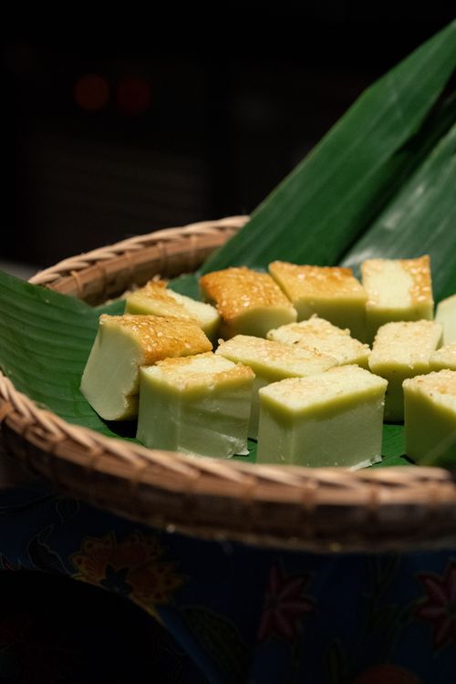 Free Delicious slices of pandan cake displayed on fresh banana leaves within a traditional winnowing basket. Stock Photo