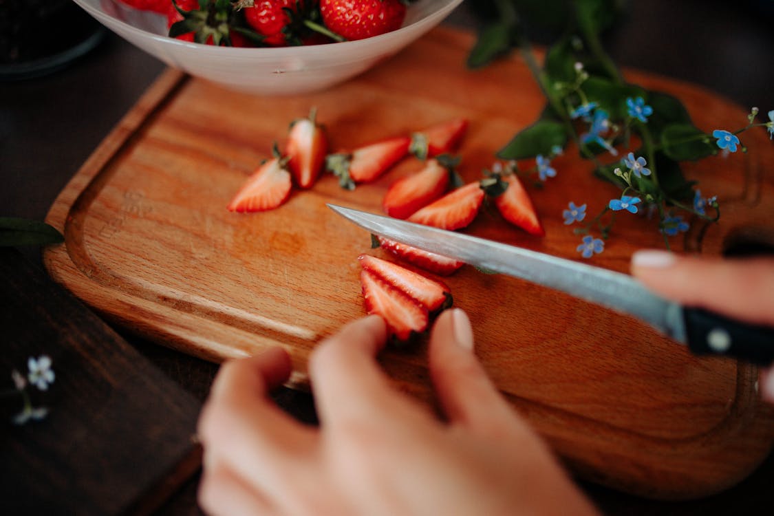 Selective Focus Photo of a Person's Hand Slicing Red Strawberries