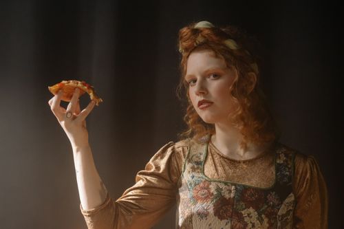 Free Artistic portrait of a woman in vintage attire holding a pizza slice. Stock Photo